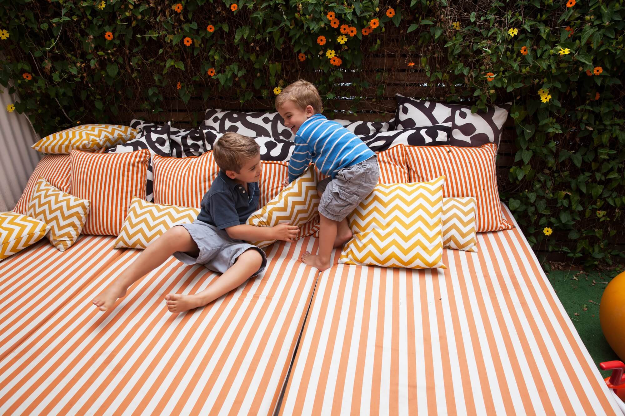 Two boys playing on outdoor furniture with cushions